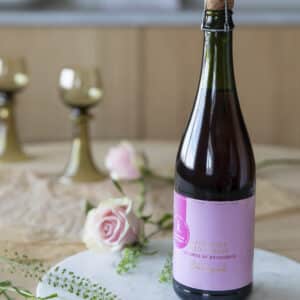Epledrikk i flaske dandert på et bord med rosa roser.