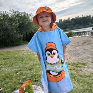 Fargerik badeponcho til barn med pingvin. Bilde på strand med barn.