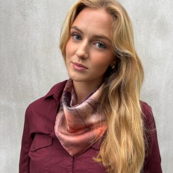 Kvinne med blondt hår og jordfarget skjerf. Grå bakgrunn.